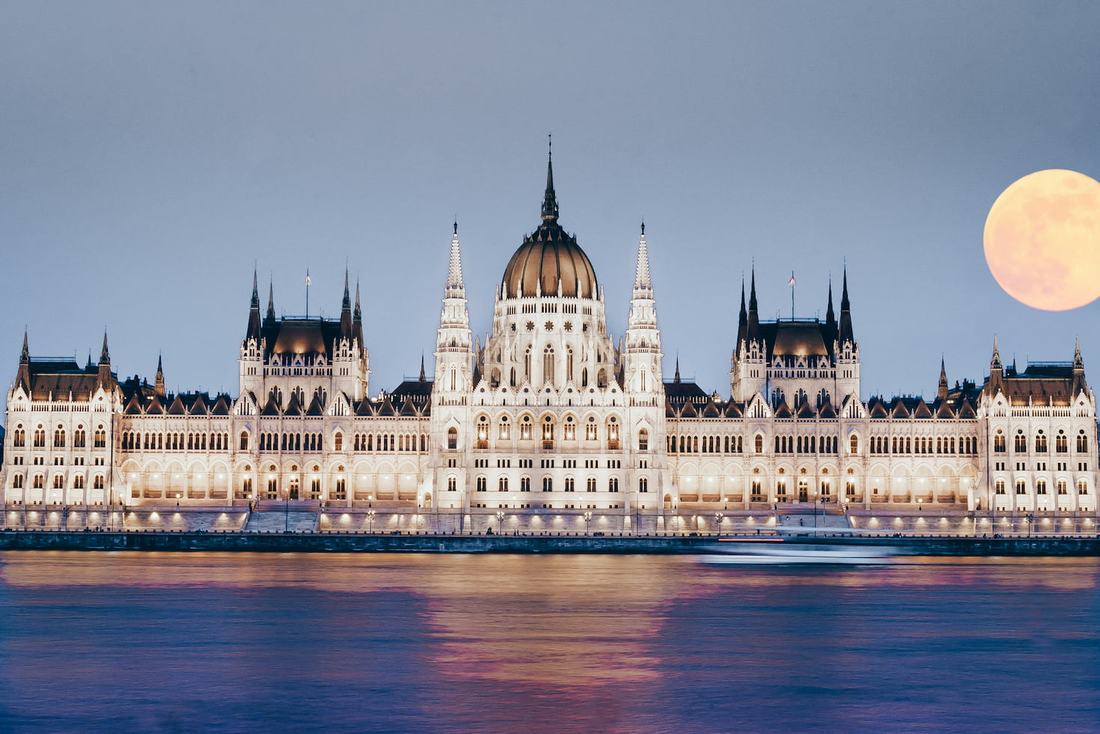 The Hungarian Parliament lit up at dusk on the Danube, with a full moon rising