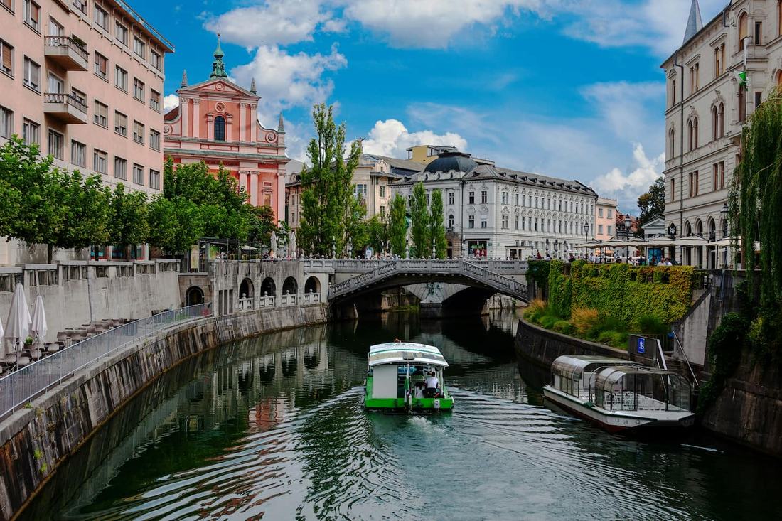 A tourist boat on the Ljubljanica river by the Triple Bridge, with the pink Franciscan Church of the Annunciation behind