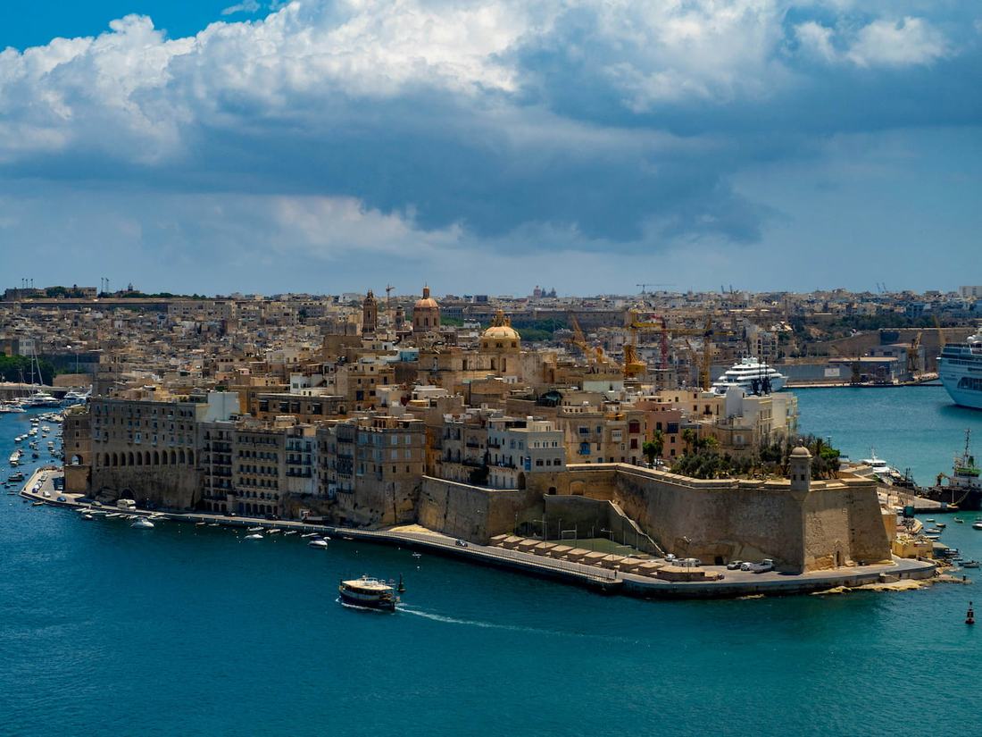 The Three Cities seen across the Grand Harbour from Valletta, with bastion walls, church domes, moored yachts and a harbour ferry