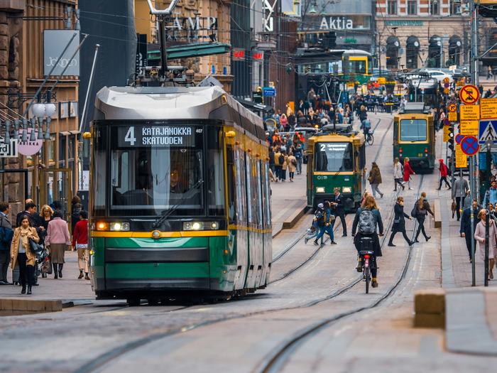 Green Helsinki tram in the city centre with cyclists and shoppers