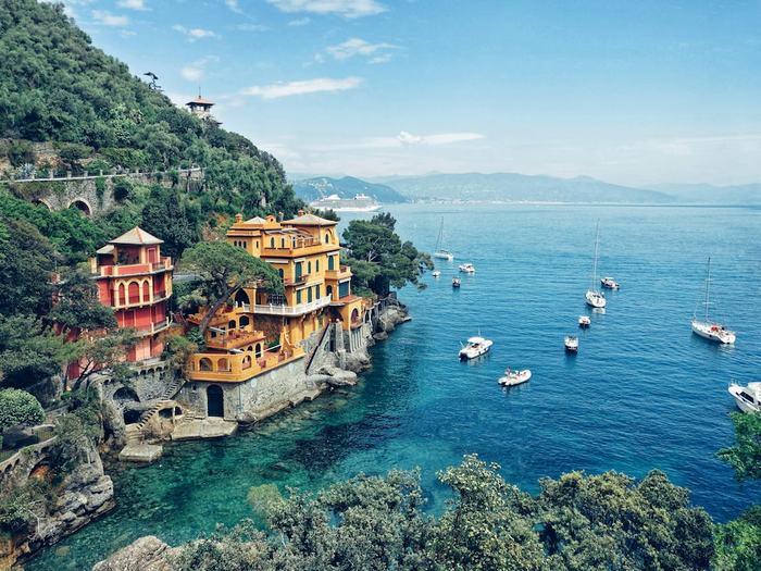 Colourful villas on a wooded cliff above a turquoise bay with sailing boats near Portofino, Liguria