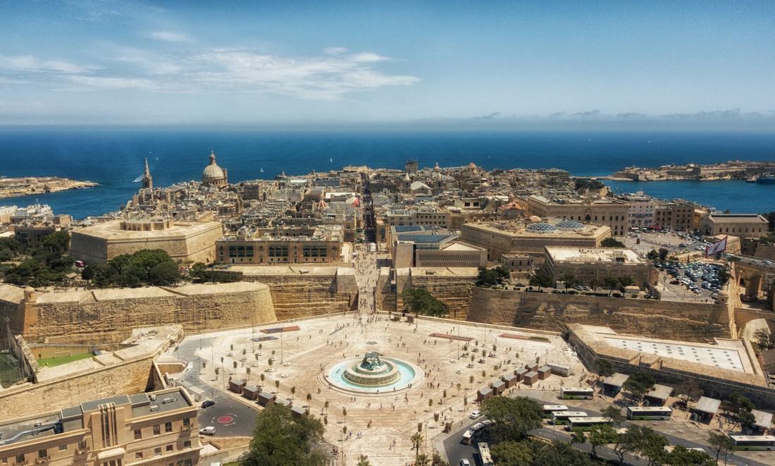 Aerial view of Valletta's City Gate square and Triton Fountain, with the bastion walls, the Carmelite church dome and the sea beyond