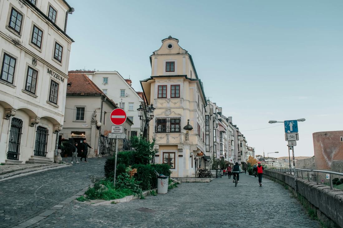 A cobbled street below Bratislava Castle with the narrow rococo House at the Good Shepherd and a cyclist riding past