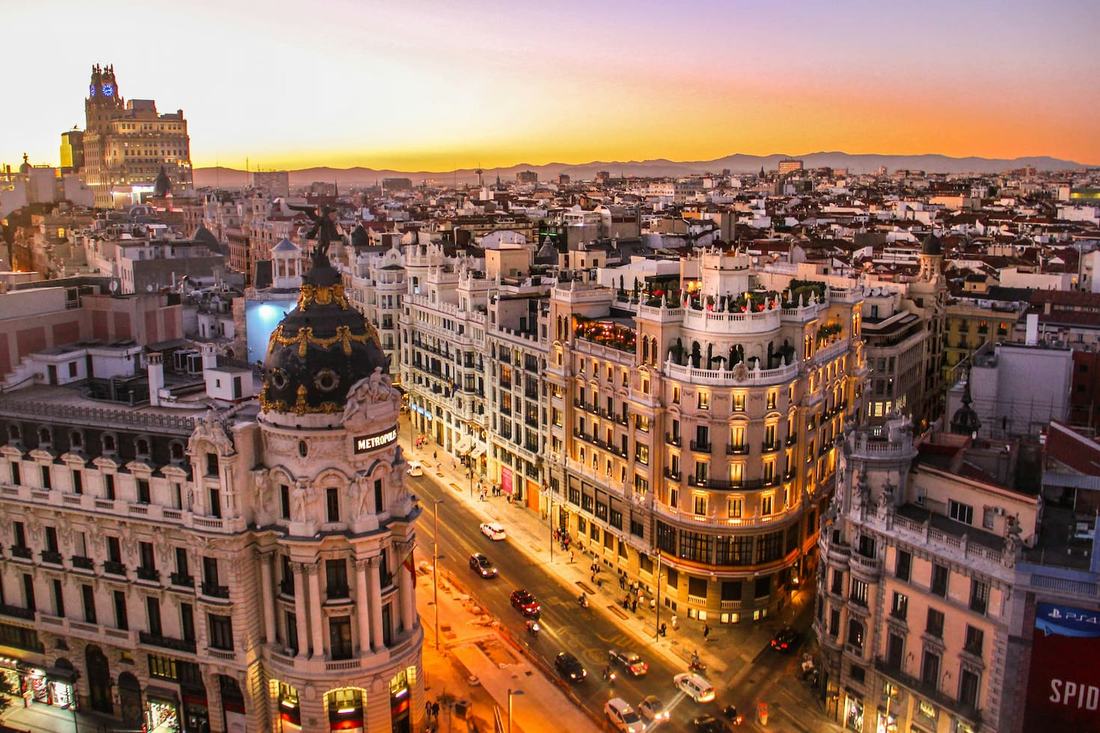 Gran Vía in Madrid at sunset, with the domed Metrópolis Building on the corner and rooftops stretching to the mountains