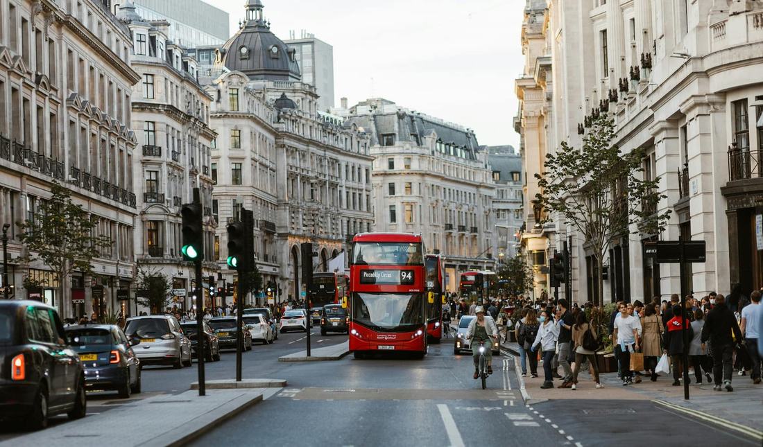 Red double-decker bus on a busy London street lined with classic stone buildings